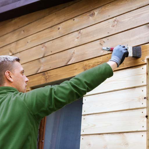 A The Honey Do Service craftsman carefully staining wood siding panels