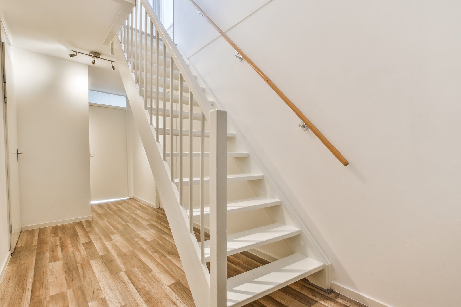 Wooden basement stairs with risers and a handrail leading to a finished lower level