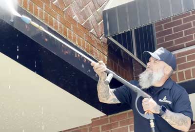 A Craftsman from The Honey Do Service, Inc. Pressure washing a retail store exterior